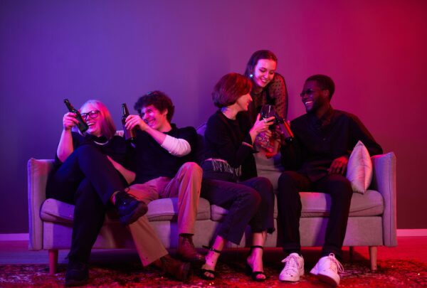 Group of young people sitting on a sofa and holding beers.