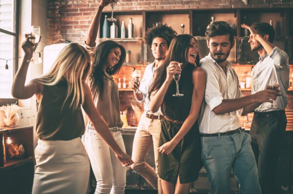 Group of people dancing in a kitchen and holding glasses of prosecco.