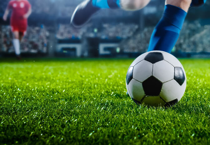 Footballer leg shot kicking a ball on a grass pitch